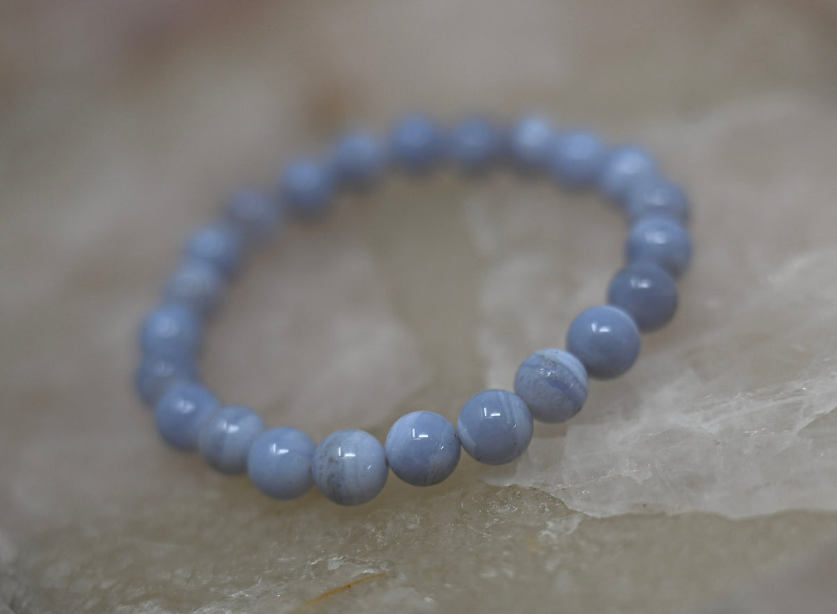 Blue lace agate bracelet with round beads on a light textured surface, photographed with a softly focused rear arc.